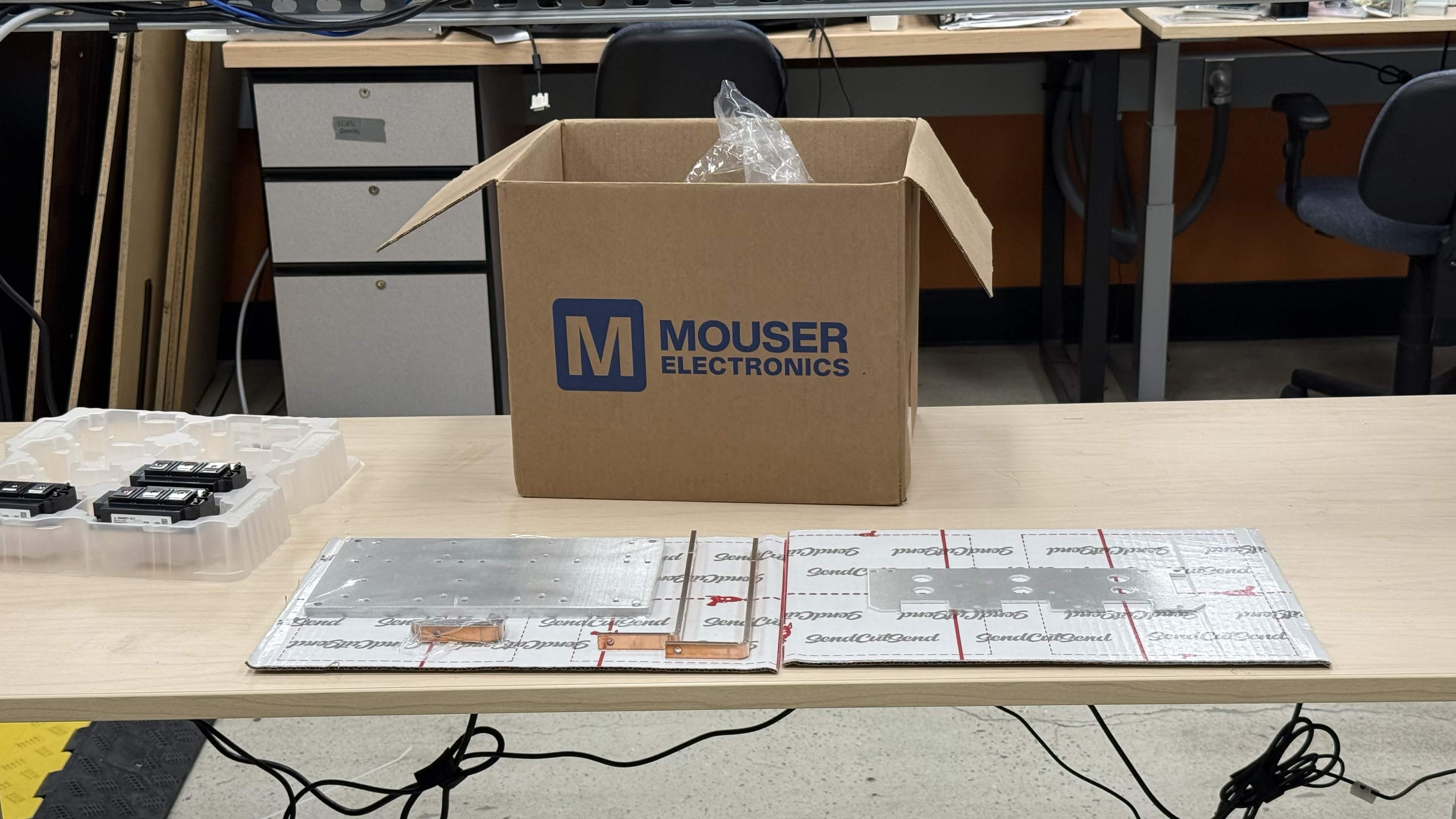 Prepared materials: IGBT modules, baseplate parts, and hardware on a workbench