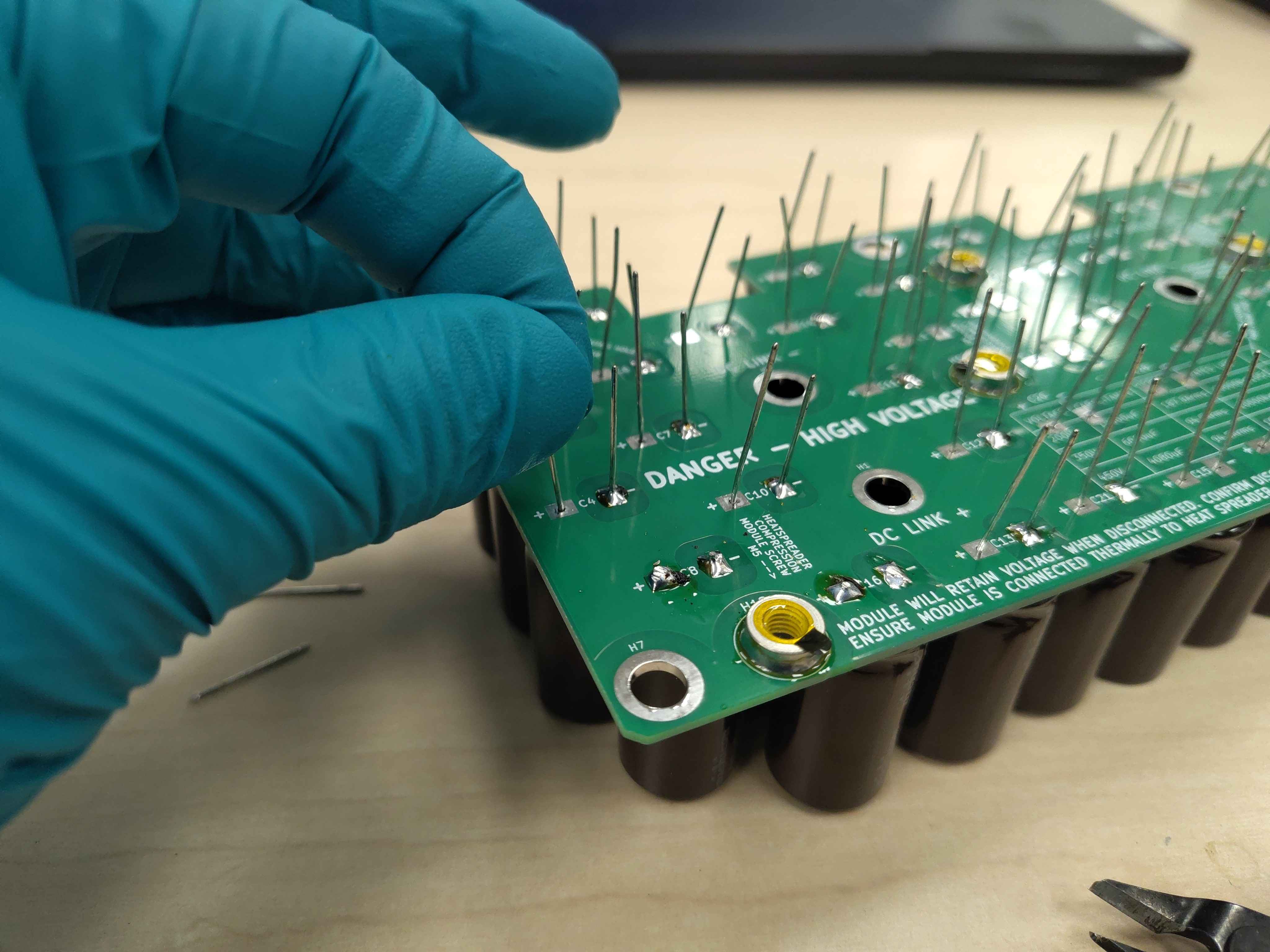 Pulling a capacitor lead from the solder side to fully seat the body against the PCB